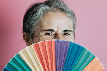 Old senior white hair woman holding an lgbti hand fan colourful background. Old people senior...
