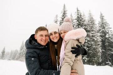 Obraz premium Portrait of playful happy family in winter forest. Mother, father and dauther playing with snow. Enjoying spending time together. Family concept