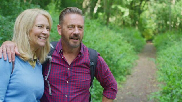 Loving mature couple walking along path through trees on hike holding hands - shot in slow motion