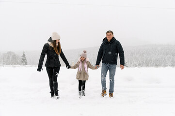 Fototapeta na wymiar Happy family have fun in winter forest. Mother, father and dauther playing with snow. Enjoying spending time together. Family concept