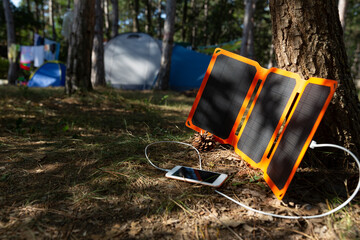 Smartphone is charging from solar battery in summer camping. Clean energy for using in hiking.