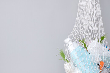 Used hygiene products in a mesh bag on a gray background. Trash with used cosmetics plastic packaging. conscious consumerism