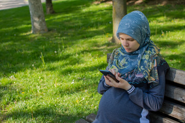 Muslim pregnant woman using smartphone in the park