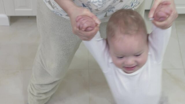 Happy baby boy holding hands of mother and hanging while mom swinging child by the arms in slow motion, mom and kid have fun together at home. High quality 4k footage
