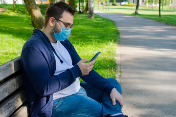 Young man with face mask using mobile phone in the park