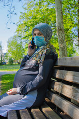 Profile view of the muslim pregnant woman wearing face mask talking on the smarphone