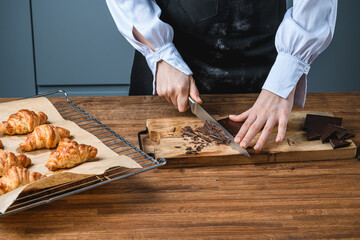 The chef slices chocolate next to croissants on a wooden table.