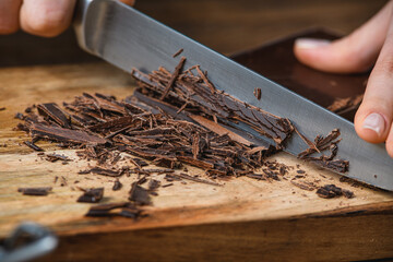 Cook cuts chocolate with a knife on a wooden table.