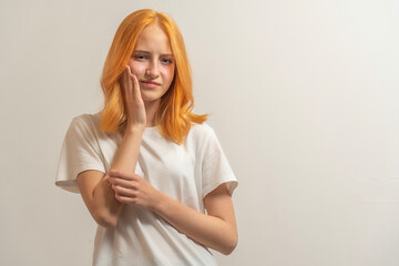 teen girl with red hair in a white t-shirt on a light background hold hand cheek ache tooth