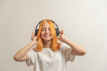 teen girl with red hair in a white t-shirt on a light background listen to music with headphones and smile