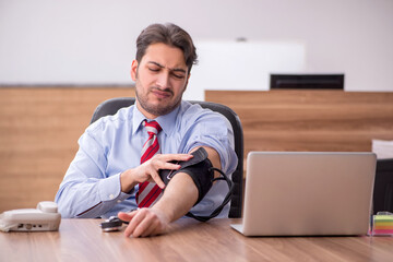 Young male employee suffering from hypertension at workplace