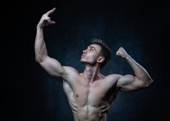 Obraz premium Young male athlete bodybuilder aestheticist posing against a dark background. Healthy lifestyle and sports concept.
