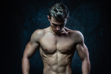 Fototapeta na wymiar Young male athlete bodybuilder aestheticist posing against a dark background. Healthy lifestyle and sports concept.