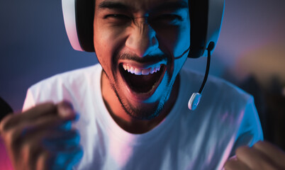 Young Asian man playing online computer video game, colorful lighting broadcast streaming live at...