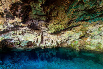 View of beautiful natural pool of crystal clear water formed in a rocky cave with stalagmites and stalagmites. Kuza cave in Zanzibar, Tanzania