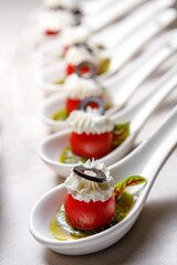 Cherry tomatoes on dessert spoons, garnished with buttercream and sliced olives.