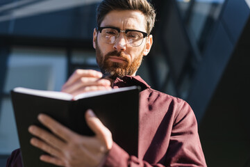 Low angle view of businessman in eyeglasses holding notebook outdoors.