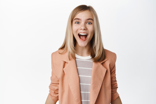 Portrait of cute girl winner, teen kid in blazer, celebrating victory, triumphing and looking happy, standing over white background
