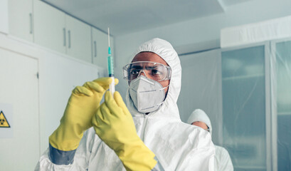 Doctor in protective suit looking and preparing syringe with vaccine in hospital