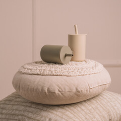 Silicone baby dishes. Two beige sippy cups with straws on knitted pillows. Creative blur and grain. Square frame instagram use