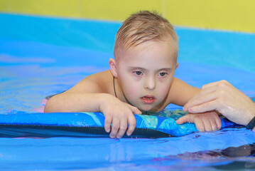 A boy with Down syndrome learns to swim in the pool, rehabilitation of disabled children, genetic anomaly, psychiatric congenital disease.
