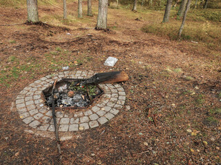 Fire place in a public park with rubbish left on the ground by people with low level of social responsibility. Littering in a nature environment.