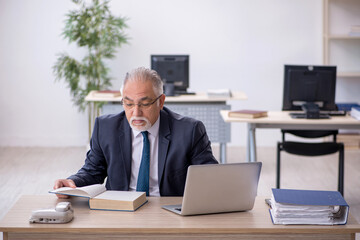 Old male employee reading book in the office