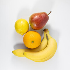 Ripe fresh bright fruits on a white background. Two bananas, an orange, a pear and a lemon. Fruits are rich in vitamins and beneficial properties