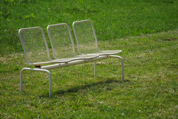 A metal bench with three places on the lawn.