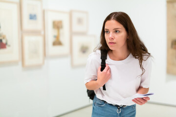 Portrait of focused girl with an information booklet studing works of art in a gallery