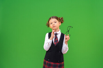 The schoolgirl looks thoughtfully into the camera. a student with glasses and a school uniform on an isolated background. copy space.