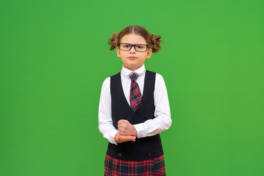 angry schoolgirl looks at the camera. school uniform with a tie. A student on a green isolated background and copy the space. study of foreign languages, courses on translation of foreign languages.