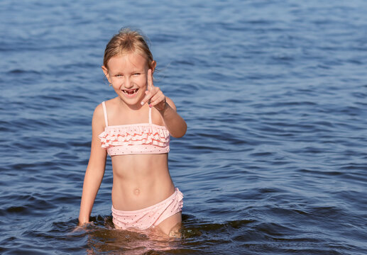 girl 6-7 years old, in a pink swimsuit, stands in the water in the sea, a portrait of a child against the background of the blue sea