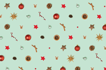 Pattern made of shiny Christmas baubles, pine cone, gold star, orange, cinnamon stick, reindeer, red decoration. Christmas ornament on pastel green background.  Bright New Year wallpaper concept.
