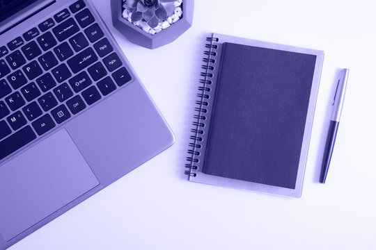 desktop flat lay with book, pc, pen and notebook toned on very pery trendy color