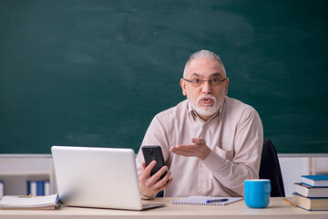 Old male teacher in front of blackboard