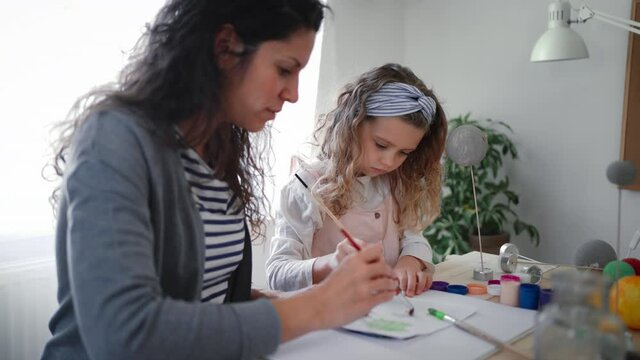 Little concentrated girl with her mother painting and making a solar system model at home, homeschooling.