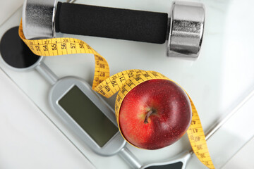 Scales, apple, measuring tape and dumbbell on white table, top view