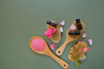 Rose essential oil and cosmetics salt with rose extract.Aromatherapy and cosmetics. Glass bottles,rose flowers and cosmetics salt on green background.Organic natural rose oil.Organic bio cosmetics