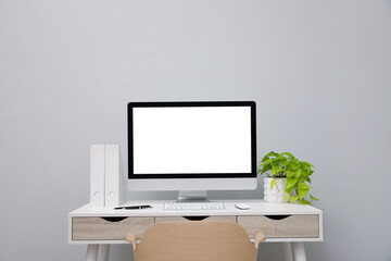Comfortable workplace with blank computer display and plant on desk near light grey wall. Space for text