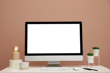 Comfortable workplace with blank computer display on desk near light brown wall. Space for text