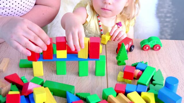 mom plays role-playing games with her daughter, small child, 2-year-old girl builds houses for characters from color blocks, concept of childhood, earlier child development, creativity, parenting