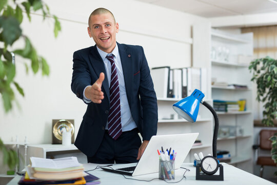 Positive European man office manager reaching out his hand for handshake and looking in camera. High quality photo