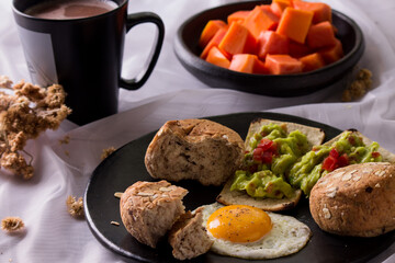 Healthy homemade breakfast with fried egg, whole grain seven grain bread, whole wheat toast with avocado and tomato, chopped papaya and hot chocolate drink.