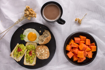 Healthy homemade breakfast with fried egg, whole grain seven grain bread, whole wheat toast with avocado and tomato, chopped papaya and hot chocolate drink.