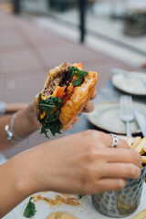 hand holding a burger and eating French fries at outdoor restaurant 