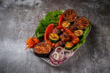 Grilled vegetables with onions and herbs in a plate against a gray stone table, vegan kebab