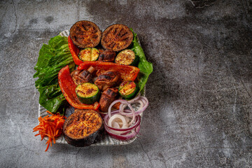 Grilled vegetables with onions and herbs in a plate against a gray stone table, vegan kebab