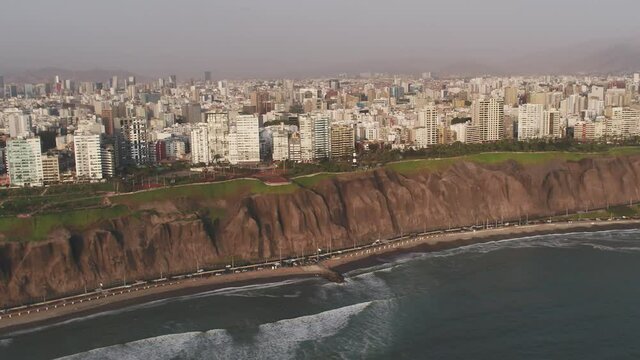 Panoramic  aerial view of Lima city, with deail of the cliff, the green coast and the buildings of the financial center of San Isidro at the background.
