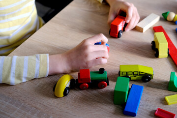 Naklejka premium close-up of child's hands holding colored wooden cubes, dominoes, child 7-9 years old builds houses, rolls cars, concept of construction game, development of creativity, fine motor skills, patience